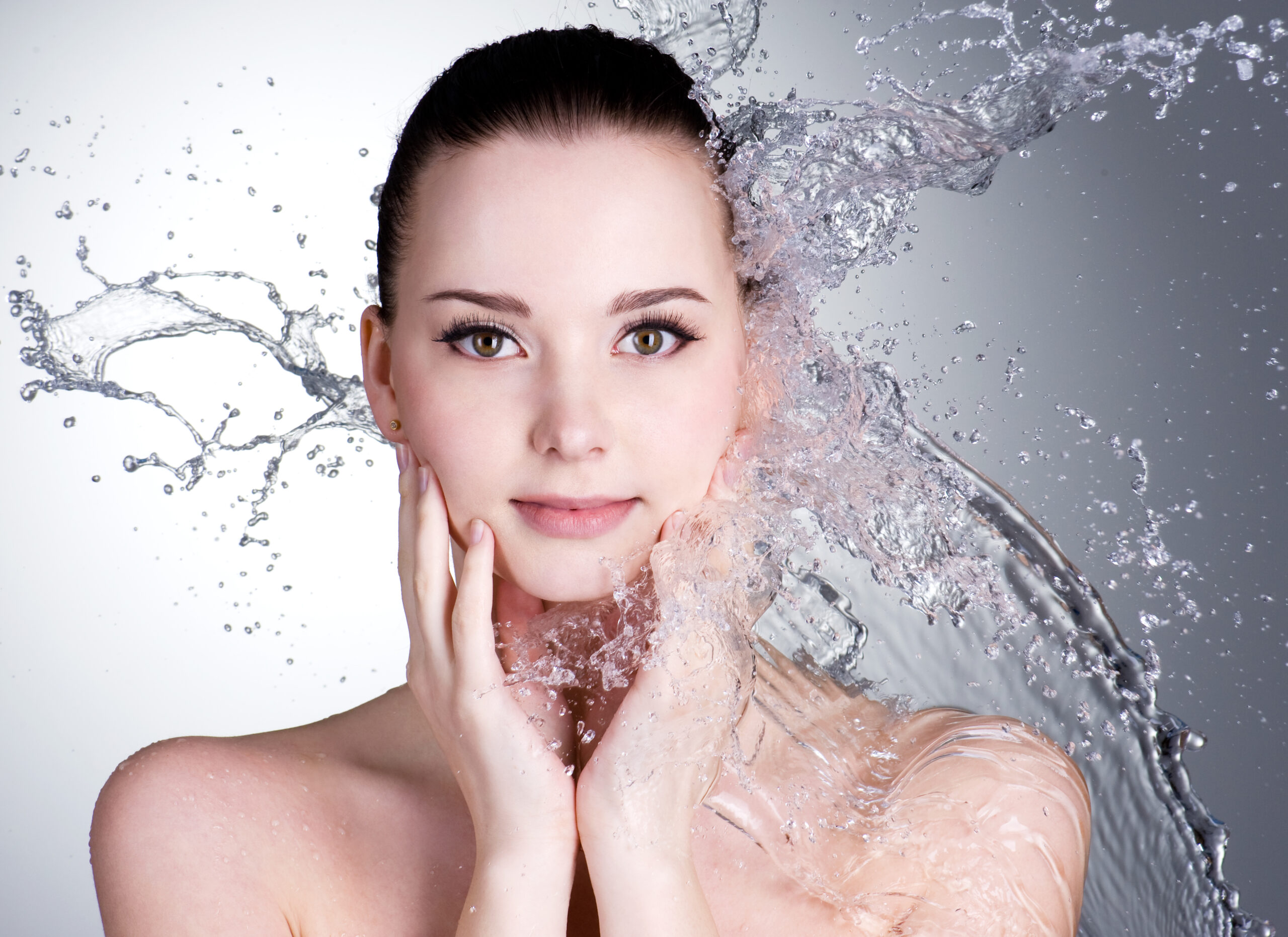 Splashes of water on the beautiful face of young woman - grey background